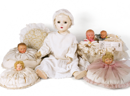 Circular fabric child-shaped pillows, reinforced to the base with thick cardboard. They are accompanied by an articulated pearl doll with inlaid eyes, dating back to the interwar period. The doll is wearing a lace dress and a cap