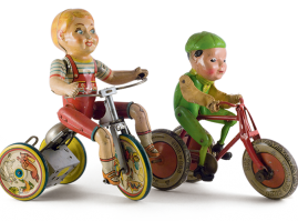 Two zinc, hand-wound tricycles with children riders: the bigger child figure comes from the american firm “Unique Art Mfg Co.” made in the 1930’s, the other figure is made of bakelite with cloth hands and comes from the english firm “Tri-ang” in the 1950’s