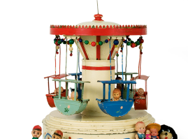 Tin folk-themed carousel from the 1930s-1940s. Small celluloid children are seated in the suspended colourful boats