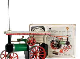 Metal steam-operated tractor made by the English company “Mamod”. Its front wheels turn by rotating the steering rod screwed onto the steam engine’s smokestack. The packaging box depicts technical details and instructions for safe operation and use