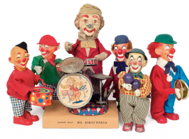 Set of wind-up clowns holding musical instruments, made of plastic and fabric and featuring a metal mechanism. The larger clown is battery-operated, plays drums and is set up on a rectangular base. Made by the Japanese company “ALPS”