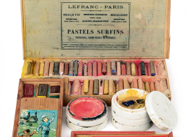 Equipment and tools for art class: Wooden water paint and crayon boxes, in a rectangular, flat shape with a printed depiction affixed. They are accompanied by two circular porcelain pots with stoppers to dissolve and mix colours