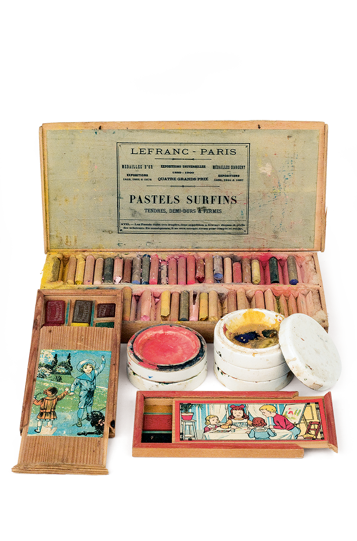 Equipment and tools for art class: Wooden water paint and crayon boxes, in a rectangular, flat shape with a printed depiction affixed. They are accompanied by two circular porcelain pots with stoppers to dissolve and mix colours