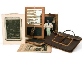 School equipment consisting of a leather handbag, printed material, two wooden slabs/blackboards with chalk and a sponge. At the centre there is an abacus and a blackboard integrated in a single wooden frame, along with a graphite pen and a natural sponge