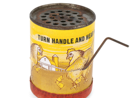 Sound-making toy, of English origin, dating back to the interwar period, with a cardboard lithograph body and a tin upper perforated surface. It depicts a mother hen, chicks and chickens on a farm that ‘cackle’ when the handle is turned