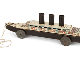 Wooden passenger ship, dragged by hand on tin wheels. Made by the English company “Tri-ang” in the 1930s-1940s. It consists of three smokestacks and its upper portion is covered by a tin lithograph