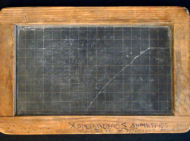 A small black slab/ blackboard with wooden frame. The frame is engraved with the student’s name