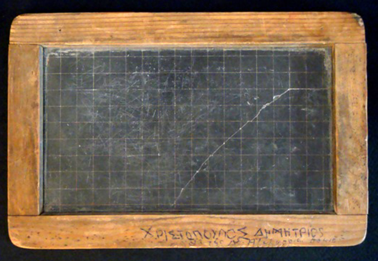 A small black slab/ blackboard with wooden frame. The frame is engraved with the student’s name